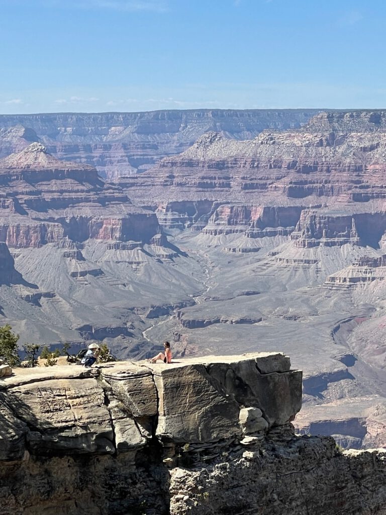 Frau sitzt auf einem spektakulären Felsvorsprung am South Rim des Grandcanyon, ein beliebter Foto-Spot bei Reisenden