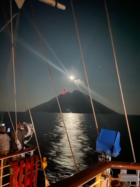 Großsegler Star Clipper kreuzt abends vor Stromboli, der Vulkan auf der Insel spuckt Lava aus